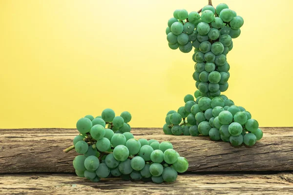 Eski bir meşe ahşap masa ve sarı duvar arka plan üzerinde güzel taze beyaz asma üzüm.
