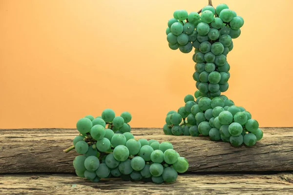 Eski bir meşe ahşap masa ve turuncu duvar arka plan üzerinde güzel taze beyaz asma üzüm.