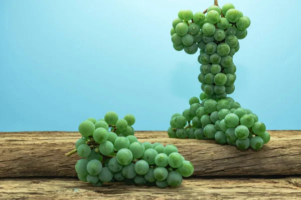 Eski bir meşe ahşap masa ve mavi duvar arka plan üzerinde güzel taze beyaz asma üzüm.