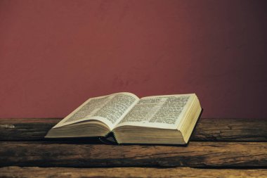 Eski meşe ahşap masa ve koyu kırmızı duvar arka plan üzerinde Güzel açık Kutsal İncil. Dini kavram.