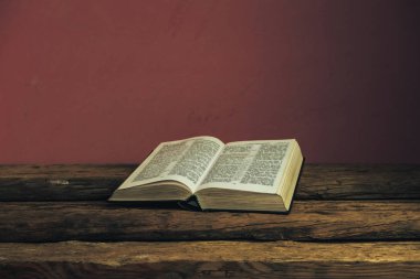 Eski meşe ahşap masa ve koyu kırmızı duvar arka plan üzerinde Güzel açık Kutsal İncil. Dini kavram.