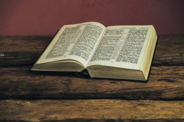 Eski meşe ahşap masa ve koyu kırmızı duvar arka plan üzerinde Güzel açık Kutsal İncil. Dini kavram.