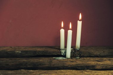 Eski bir meşe ahşap masa ve kırmızı duvar arka plan üzerinde güzel üç beyaz yanmış mumlar. 
