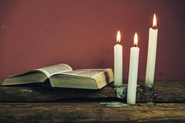 Güzel açık İncil ve eski bir meşe ahşap masa ve kırmızı duvar arka plan üzerinde üç beyaz yanmış mumlar. 