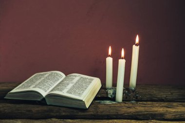 Güzel açık İncil ve eski bir meşe ahşap masa ve kırmızı duvar arka plan üzerinde üç beyaz yanmış mumlar. 