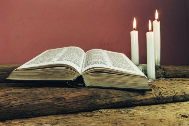 Yakın güzel açık İncil ve eski bir meşe ahşap masa ve kırmızı duvar arka plan üzerinde üç beyaz yanmış mumlar kadar. 