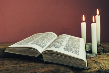 Yakın güzel açık İncil ve eski bir meşe ahşap masa ve kırmızı duvar arka plan üzerinde üç beyaz yanmış mumlar kadar. 