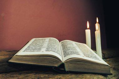 Yakın güzel açık İncil ve eski bir meşe ahşap masa ve kırmızı duvar arka plan üzerinde üç beyaz yanmış mumlar kadar. 