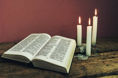 Yakın güzel açık İncil ve eski bir meşe ahşap masa ve kırmızı duvar arka plan üzerinde üç beyaz yanmış mumlar kadar. 