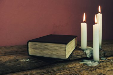Güzel kapalı kutsal İncil ve eski bir meşe ahşap masa ve kırmızı duvar arka plan üzerinde üç beyaz yanmış mumlar. 