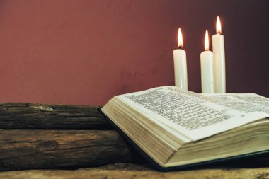 Yakın güzel açık İncil ve eski bir meşe ahşap masa ve kırmızı duvar arka plan üzerinde üç beyaz yanmış mumlar kadar. 