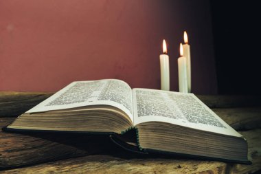 Yakın güzel açık İncil ve eski bir meşe ahşap masa ve kırmızı duvar arka plan üzerinde üç beyaz yanmış mumlar kadar. 