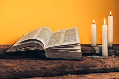 Güzel açık İncil ve eski bir meşe ahşap masa ve sarı duvar arka plan üzerinde üç beyaz yanmış mumlar. 