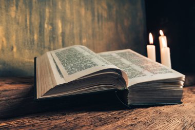 Eski bir meşe ahşap masa ve gri altın duvar arka plan üzerinde güzel açık İncil ve üç beyaz yanmış mumlar kadar kapatın. 