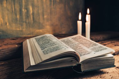 Eski bir meşe ahşap masa ve gri altın duvar arka plan üzerinde güzel açık İncil ve üç beyaz yanmış mumlar kadar kapatın. 