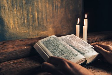 Eski bir meşe ahşap masa ve altın duvar backgroud üzerinde İncil okuma bir masada oturan adam kapatın