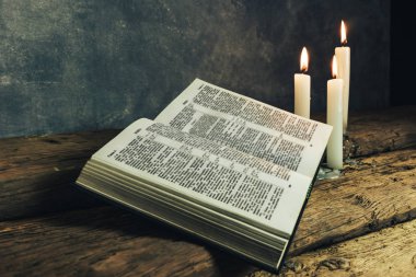 Güzel açık İncil ve eski bir meşe ahşap masa ve koyu gri duvar arka plan üzerinde üç beyaz yanmış mumlar. 