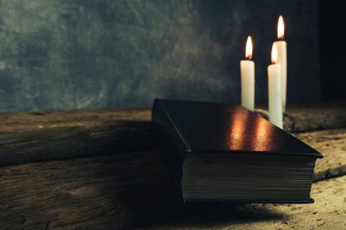 Güzel kapalı kutsal İncil ve eski bir meşe ahşap masa ve gri duvar arka plan üzerinde üç beyaz yanmış mumlar. 