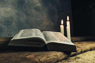 Güzel açık İncil ve eski bir meşe ahşap masa ve koyu gri duvar arka plan üzerinde üç beyaz yanmış mumlar. 