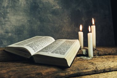 Güzel açık İncil ve eski bir meşe ahşap masa ve koyu gri duvar arka plan üzerinde üç beyaz yanmış mumlar. 