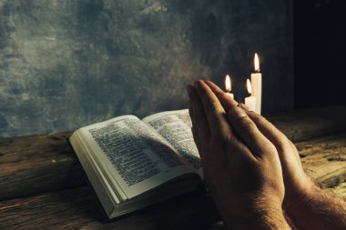 Eski bir meşe ahşap masa ve gri duvar backgroud üzerinde İncil okuma bir masada oturan adam kapatın