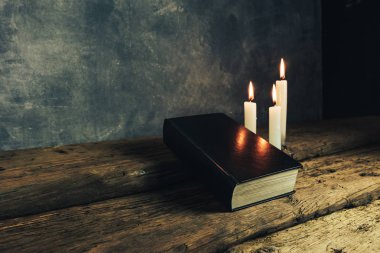 Güzel kapalı kutsal İncil ve eski bir meşe ahşap masa ve gri duvar arka plan üzerinde üç beyaz yanmış mumlar. 