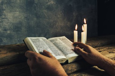 Eski bir meşe ahşap masa ve gri duvar backgroud üzerinde İncil okuma bir masada oturan adam kapatın