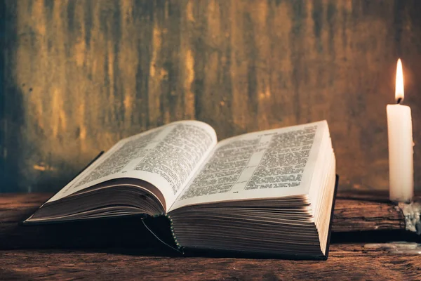 Eski bir meşe ahşap masa ve gri altın duvar arka plan üzerinde güzel açık İncil ve üç beyaz yanmış mumlar kadar kapatın. 