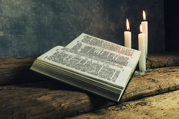 Güzel açık İncil ve eski bir meşe ahşap masa ve koyu gri duvar arka plan üzerinde üç beyaz yanmış mumlar. 
