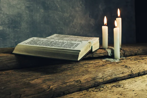 Güzel açık İncil ve eski bir meşe ahşap masa ve koyu gri duvar arka plan üzerinde üç beyaz yanmış mumlar. 