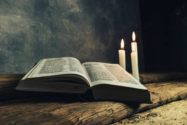 Güzel açık İncil ve eski bir meşe ahşap masa ve koyu gri duvar arka plan üzerinde üç beyaz yanmış mumlar. 