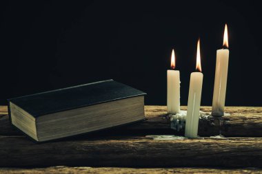 Güzel kapalı kutsal İncil ve eski bir meşe ahşap masa ve siyah arka plan üzerinde üç beyaz yanmış mumlar. 