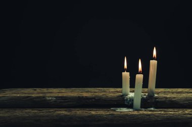 Eski bir meşe ahşap masa ve siyah arka plan üzerinde güzel üç beyaz yanmış mumlar. 