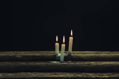 Eski bir meşe ahşap masa ve siyah arka plan üzerinde güzel üç beyaz yanmış mumlar. 