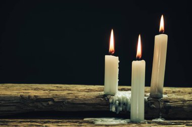 Eski bir meşe ahşap masa ve siyah arka plan üzerinde güzel üç beyaz yanmış mumlar. 