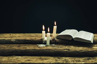 Güzel açık İncil ve eski bir meşe ahşap masa ve koyu arka plan üzerinde yanmış mumlar. 
