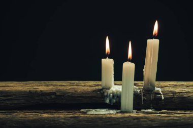Eski bir meşe ahşap masa ve siyah arka plan üzerinde güzel üç beyaz yanmış mumlar. 