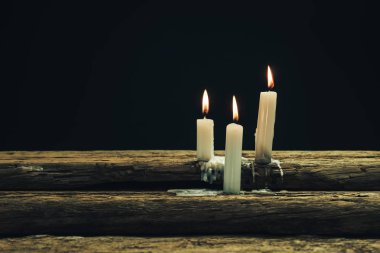 Eski bir meşe ahşap masa ve siyah arka plan üzerinde güzel üç beyaz yanmış mumlar. 