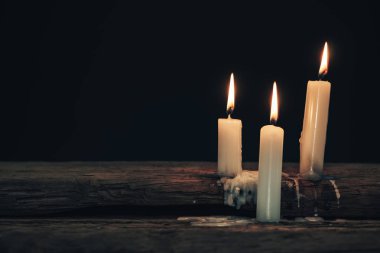 Eski bir meşe ahşap masa ve siyah arka plan üzerinde güzel üç beyaz yanmış mumlar. 