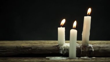 Eski bir meşe ahşap masa ve siyah arka plan üzerinde güzel üç beyaz yanmış mumlar. 