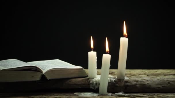 美丽的开放式圣经和烧蜡烛在一个古老的橡木表和黑暗的背景 — 图库视频影像