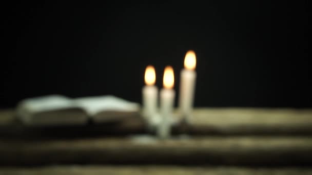 美しいオープン聖書と古いオーク材の木製のテーブルと暗い背景に焼かれたキャンドル — ストック動画