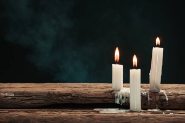 Eski bir meşe ahşap masada güzel üç beyaz yanmış mumlar. Mavi ve kırmızı dumanArka Plan