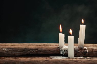 Eski bir meşe ahşap masada güzel üç beyaz yanmış mumlar. Mavi ve kırmızı dumanArka Plan