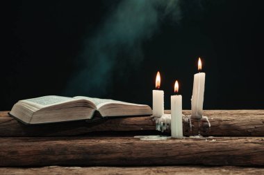 Güzel açık İncil ve eski bir meşe ahşap masada mumlar yandı. Dumanın arka planı.