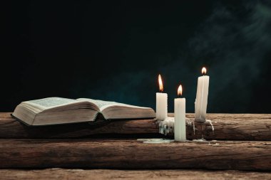 Güzel açık İncil ve eski bir meşe ahşap masada mumlar yandı. Dumanın arka planı.