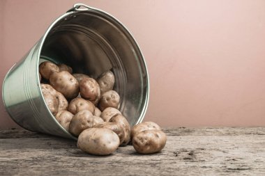 Eski bir meşe ahşap masa ve güzel kırmızı duvar arka plan üzerinde gümüş sepet taze patates.