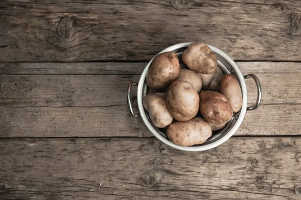 Fresh potato in silver basket on a old oak wooden table and beautiful background. Top view.