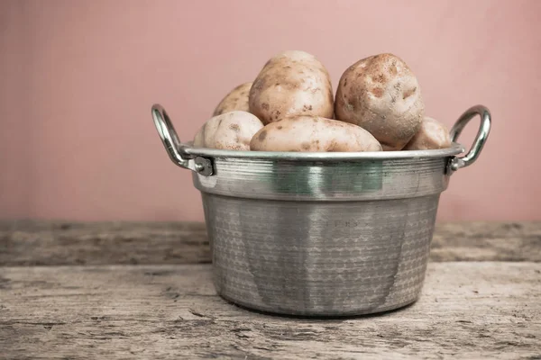 Fresh potato in silver basket on a old oak wooden table and beautiful red wall background.