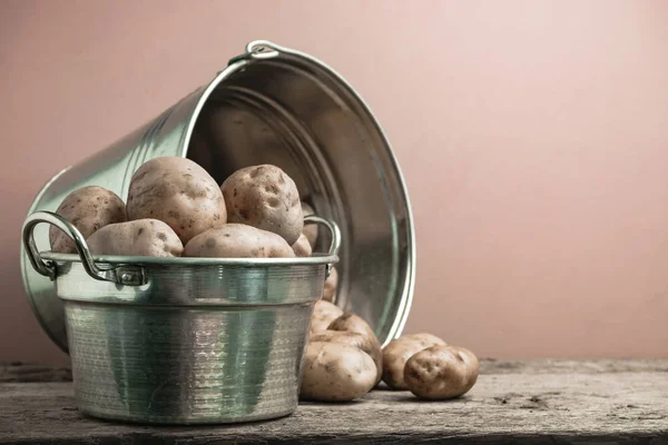 Fresh potato in silver basket on a old oak wooden table and beautiful red wall background.